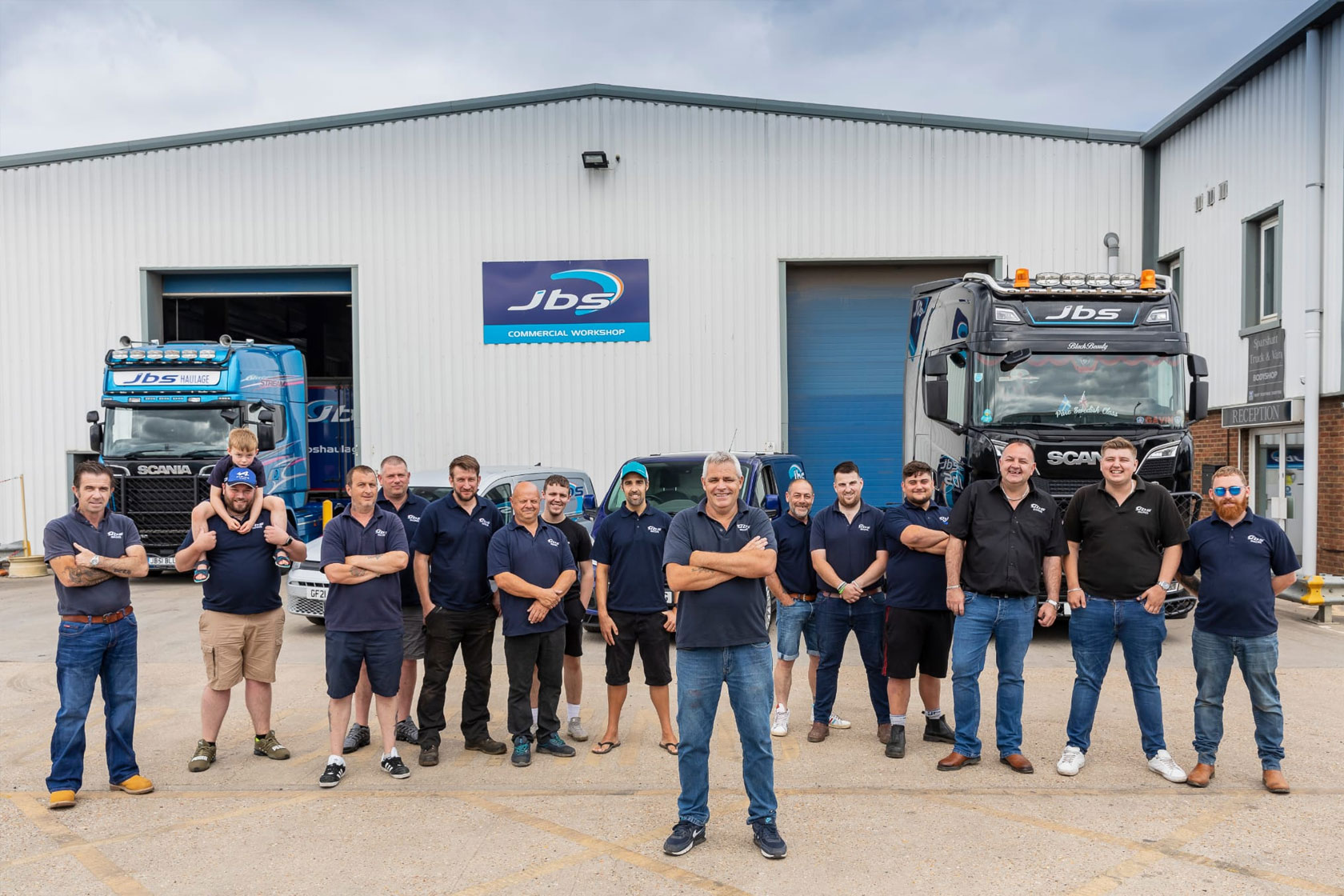 All of our team in a line stood next to each other posing for a photo i n front of the JBS workshop