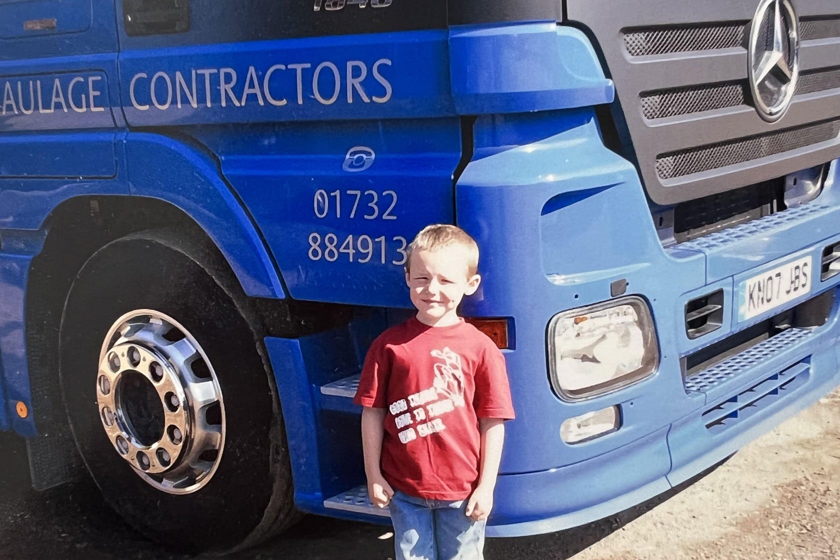 A picture of a boy stood in front of a blue Sparchatts Mercedes Truck