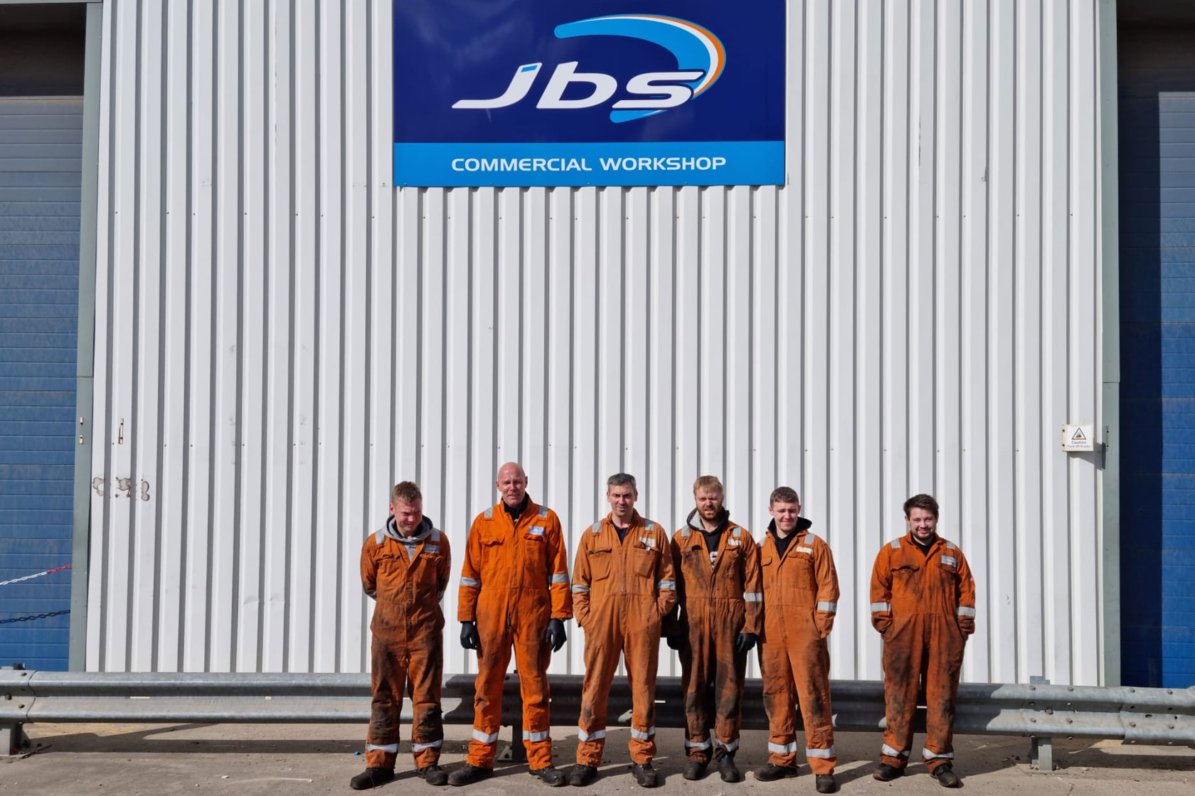 Technician Team lined up in orange jumpsuits in front of the JBS workshop