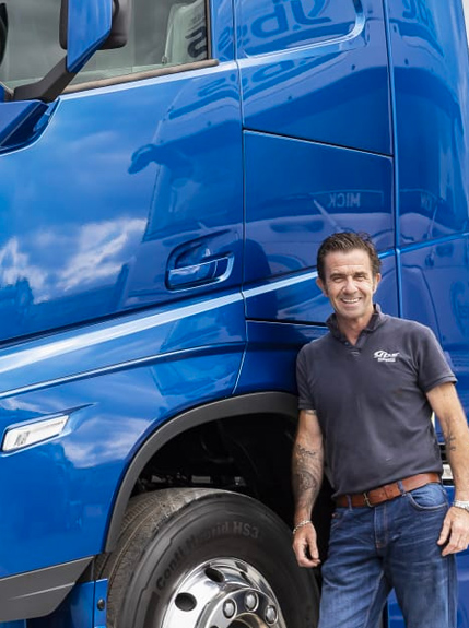 A Portrait photo of Tony, Advanced Driver stood in beside the door of a Blue JBS truck 